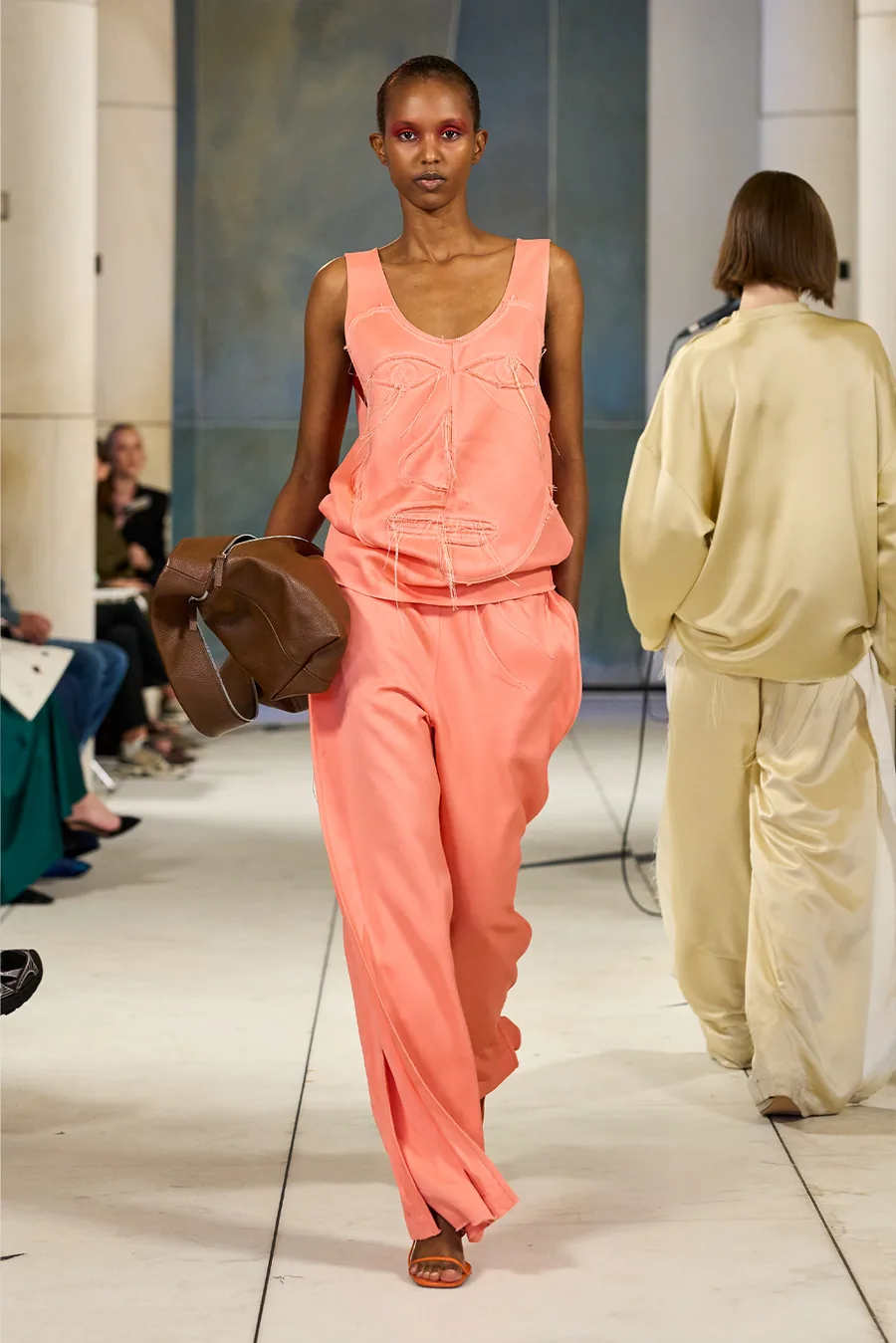 SHOWstudio, Litkovska S/S 27 STRICHA: Model in korallfarbenem Oberteil und weiter Hose mit brauner Ledertasche