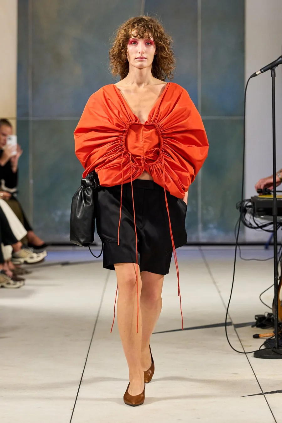 SHOWstudio, Litkovska S/S 27 STRICHA: Model in einem gerafften orangen Oberteil und schwarzen Shorts mit langen Bändern